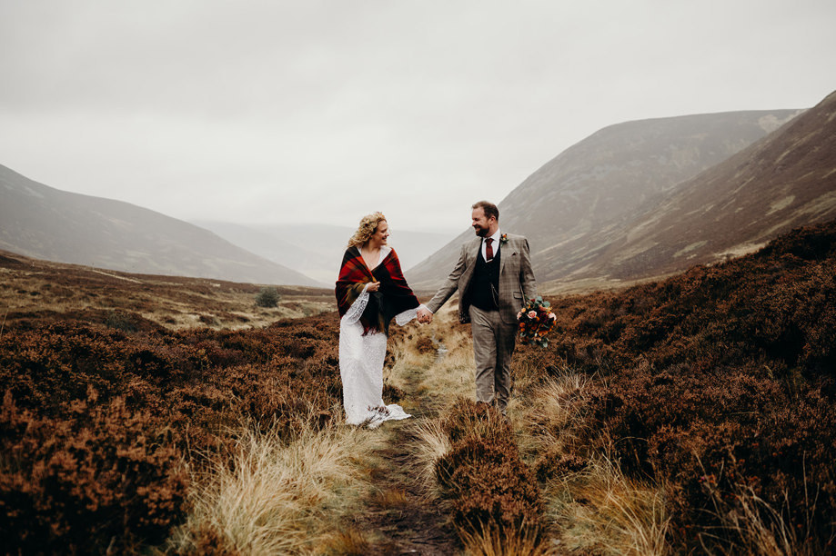 Bride and groom walk through wilderness with misty hills in background